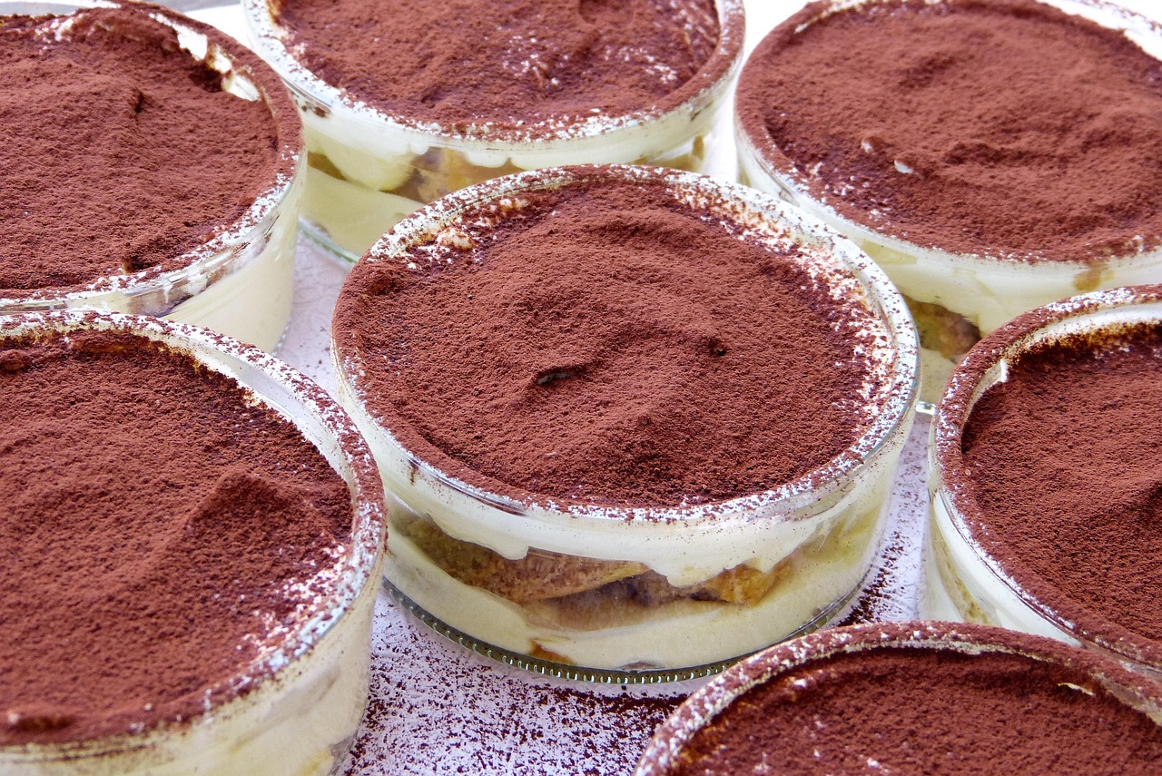 Tiramisù senza uova presentato in una ciotola decorata con cacao e chicchi di caffè.
