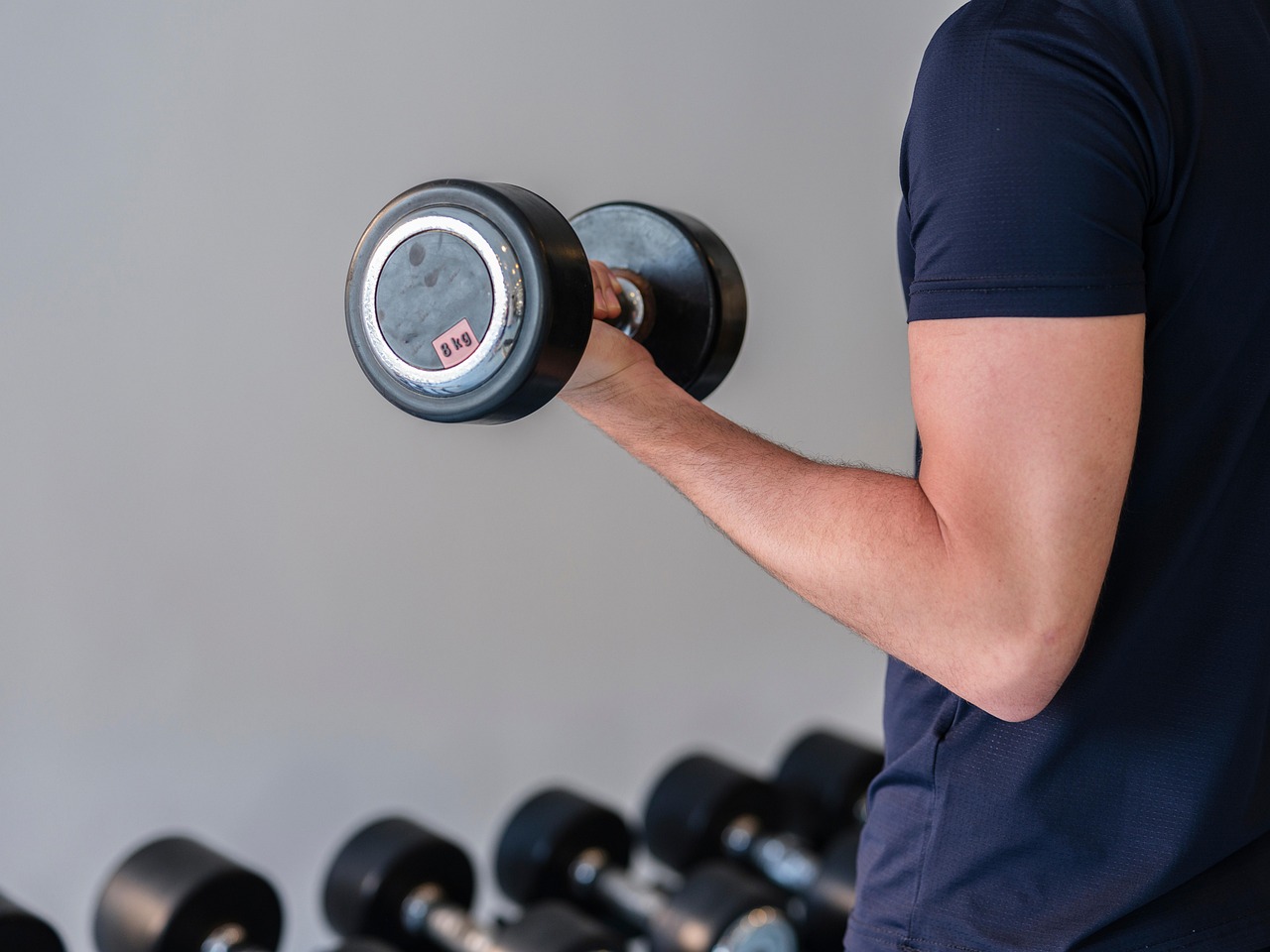 Esercizio per bicipiti con attrezzi, personal trainer mostra tecnica corretta in palestra.