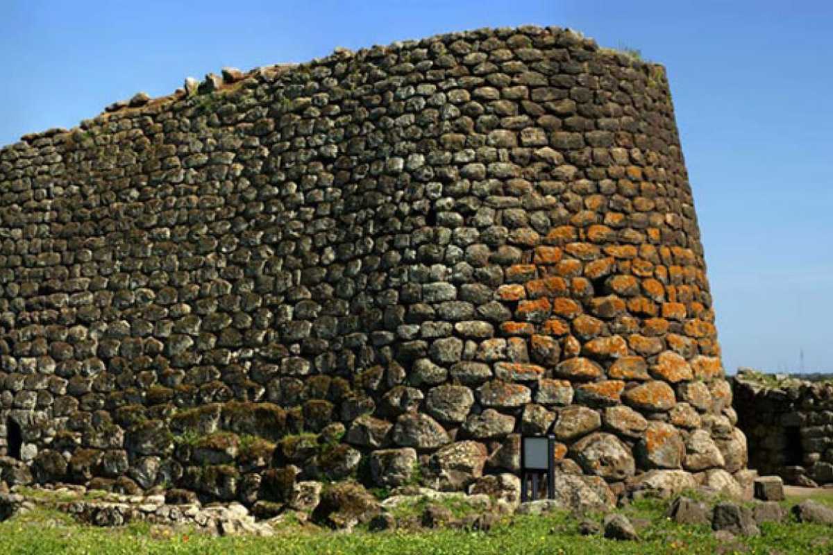 Borgo sardo con nuraghe ben conservato, circondato da case tradizionali e natura.